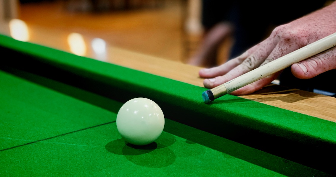 A close up of a customer's hands as they line up their shot at the pool table.